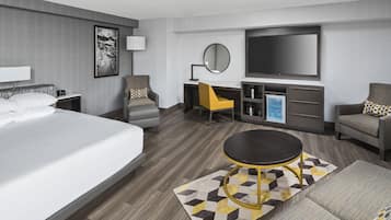Moderni hotellihuone, jossa on suuri sänky, työpöytä, televisio ja oleskelualue.