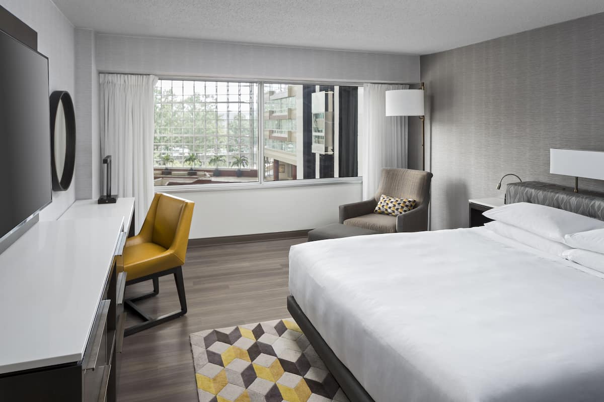 Ein Hotelzimmer mit Bett, Schreibtisch, Stuhl, Lampe und Blick ins Freie.