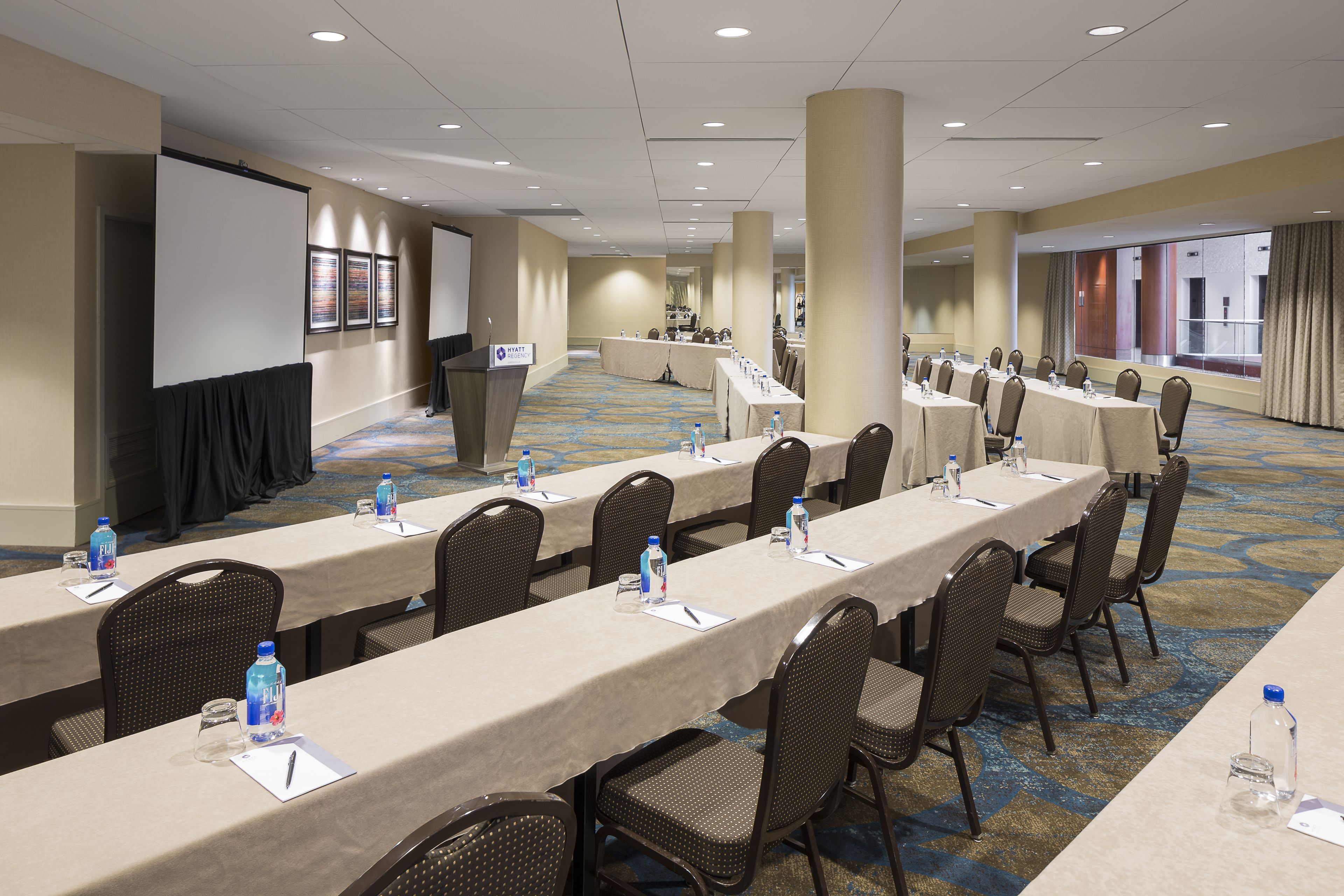 A conference room with long tables, chairs, and a projector screen.