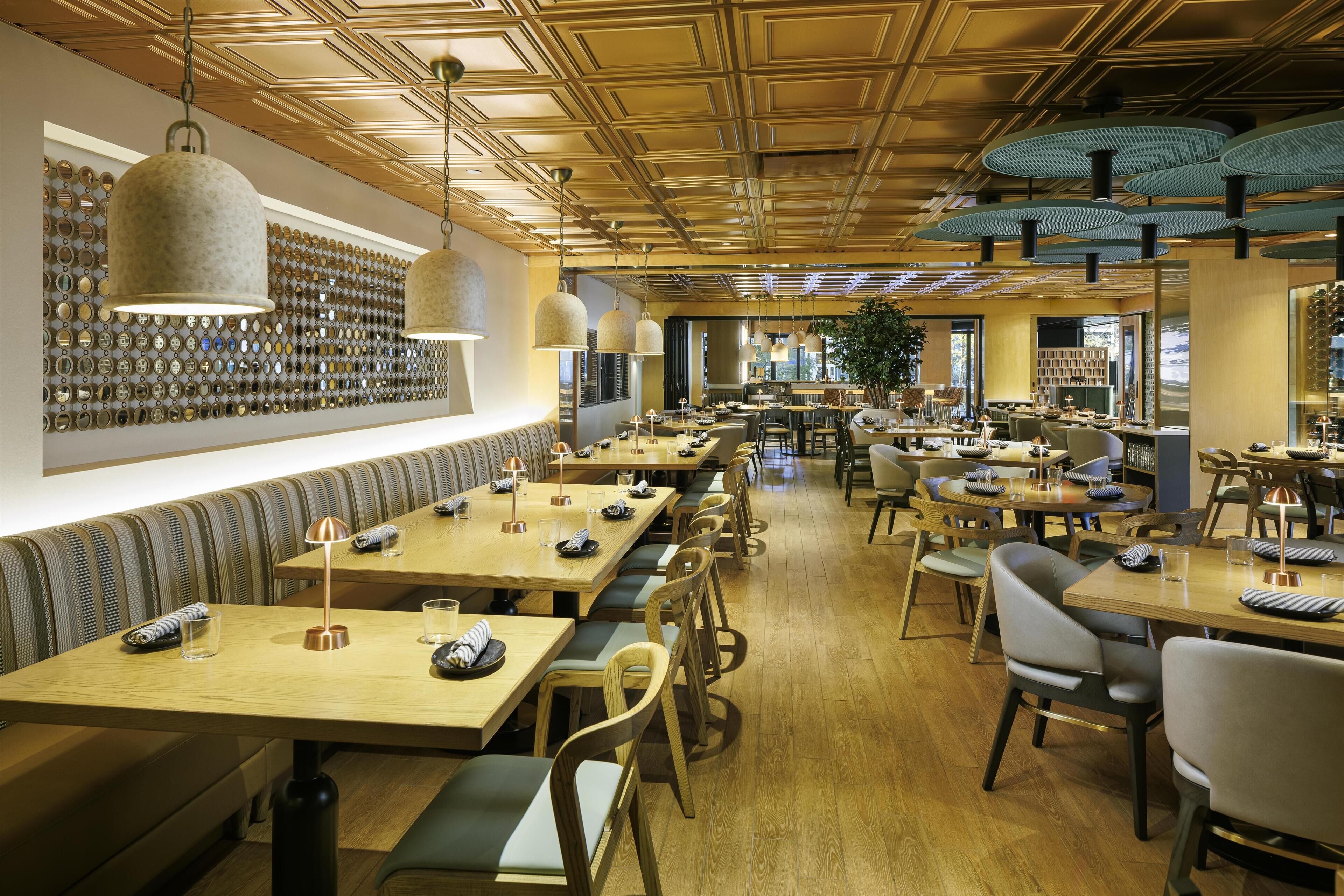 A restaurant with long wooden tables, cushioned benches, and hanging pendant lights.