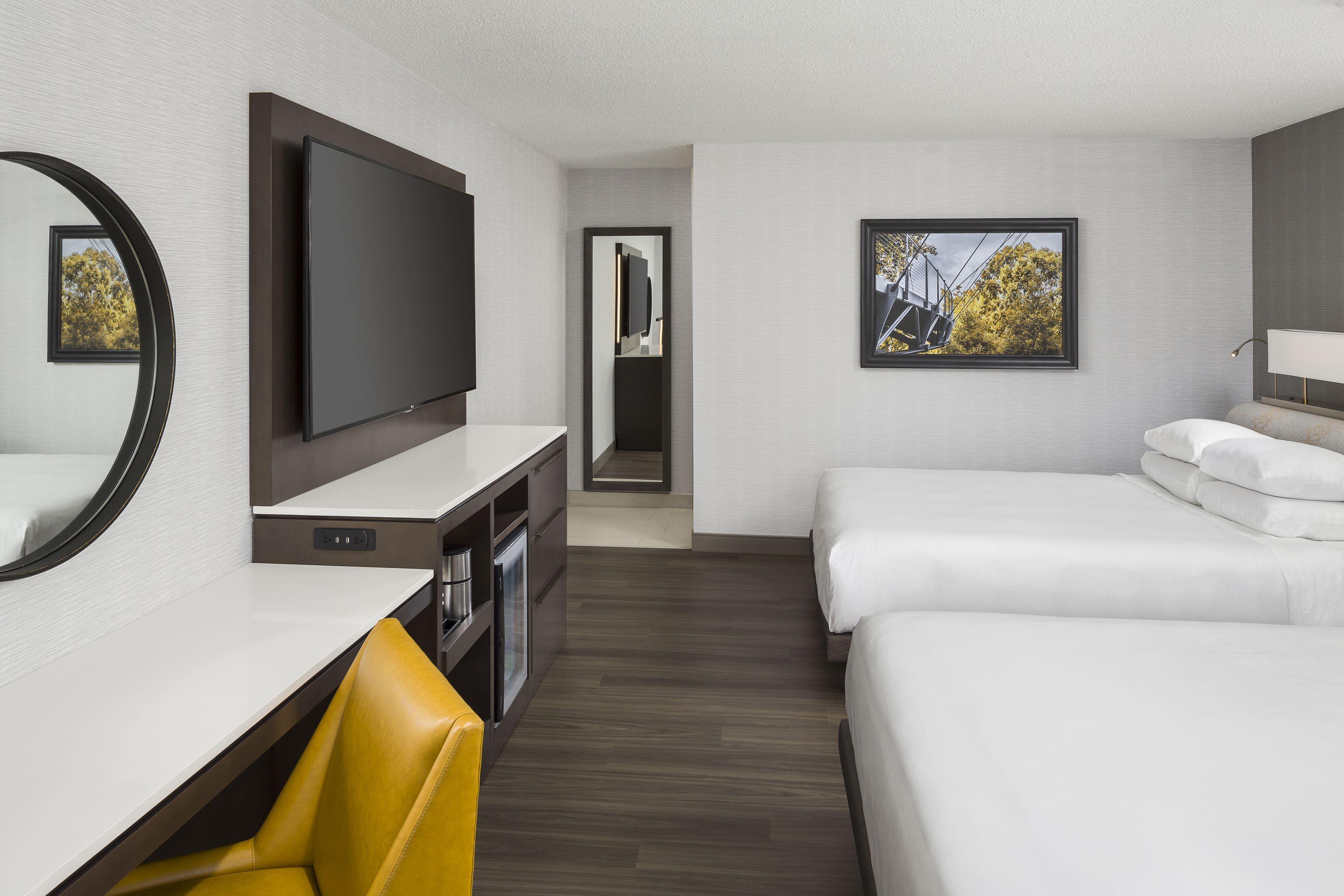 A hotel room with a flat-screen TV, a desk with a chair, two beds, and a framed picture on the wall.
