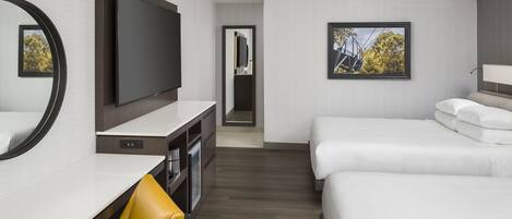 A hotel room with a flat-screen TV, a desk with a chair, two beds, and a framed picture on the wall.
