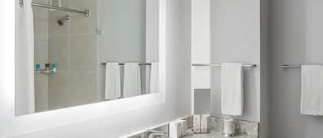 A modern bathroom with a large mirror, a shower, a toilet, and a sink with marble countertop.