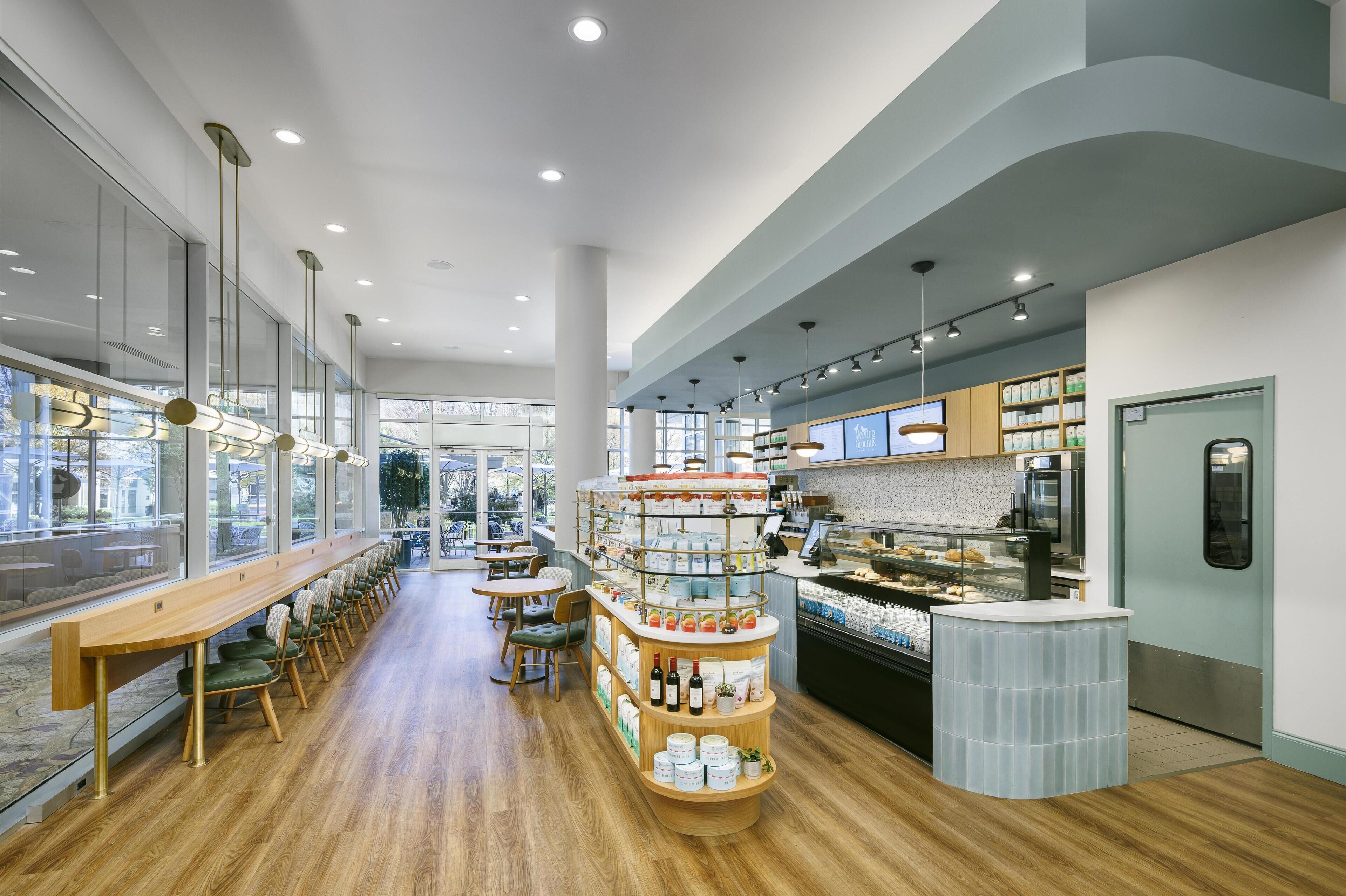 Un café moderne avec un long comptoir en bois, un espace salon et un présentoir où sont exposés les différents plats proposés.