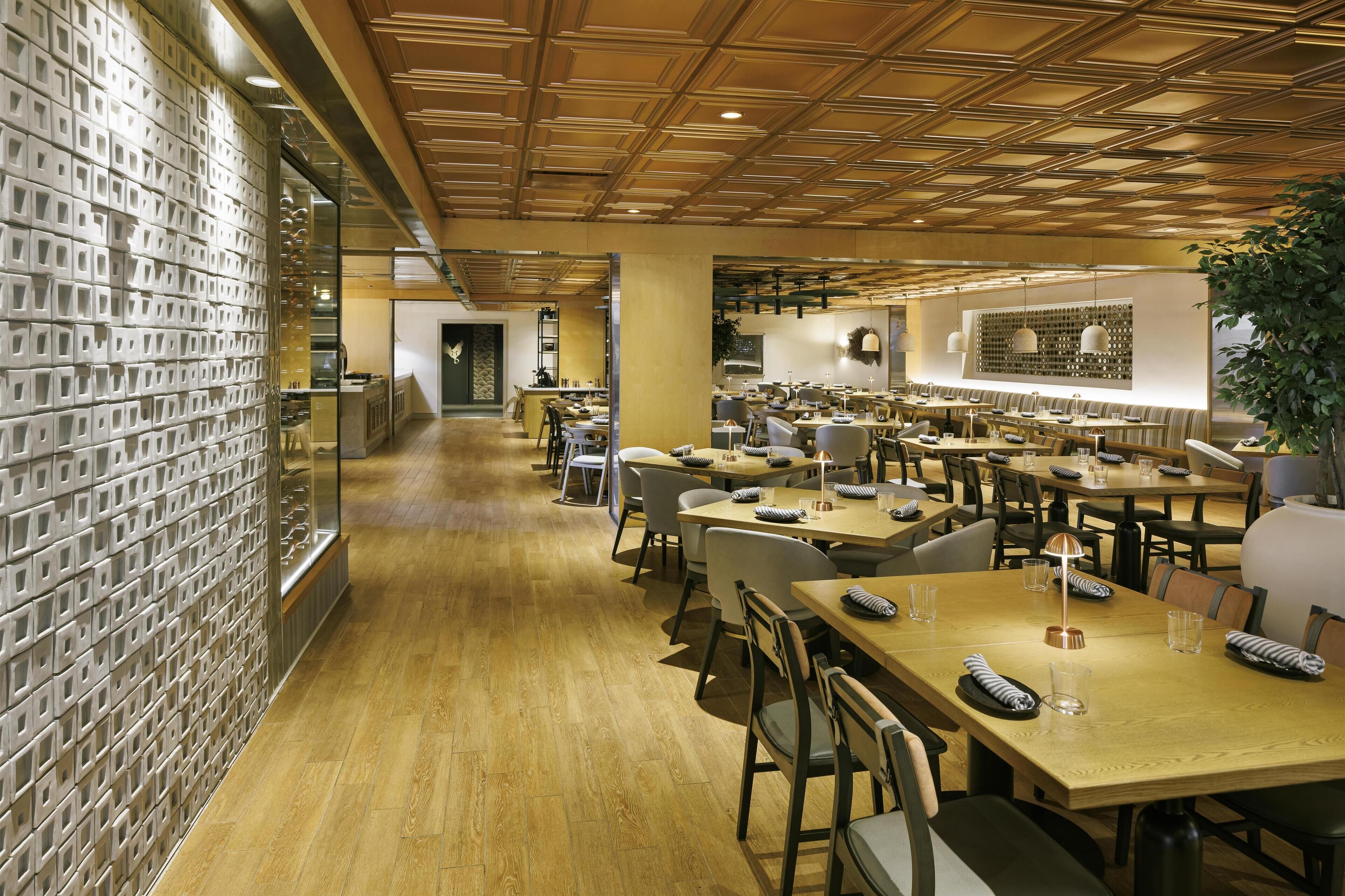 Een ruim restaurant met meerdere eettafels en stoelen, een houten plafond en een wand met een uniek patroon.