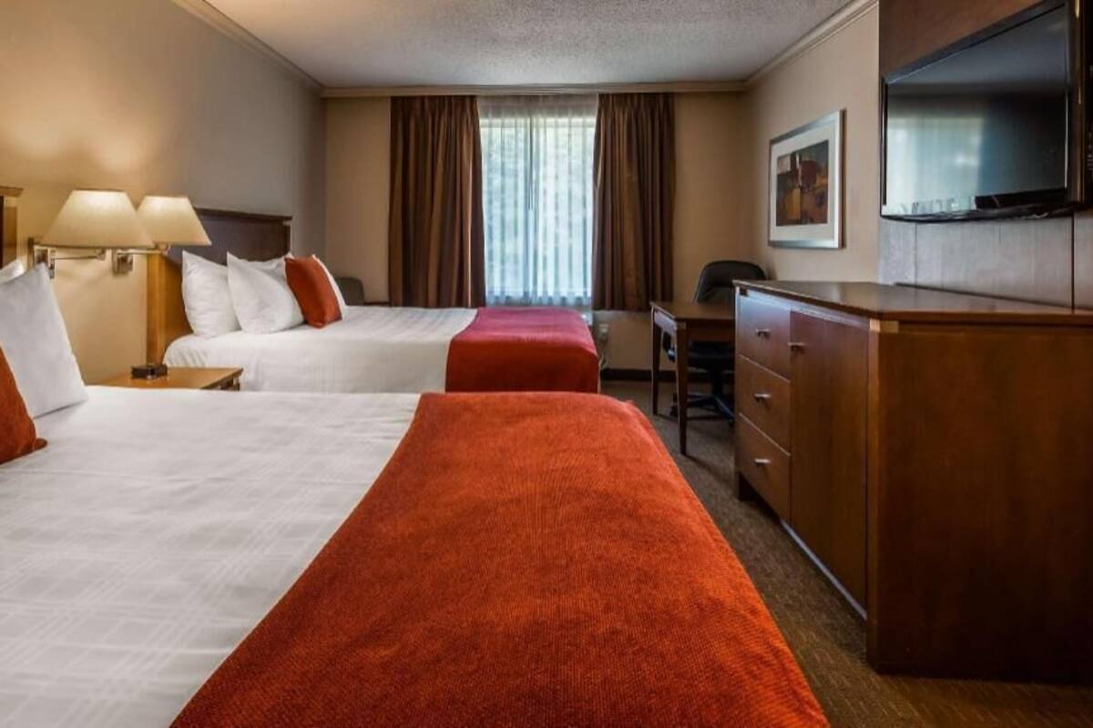 A hotel room with two beds, a desk, a television, and a window with curtains.