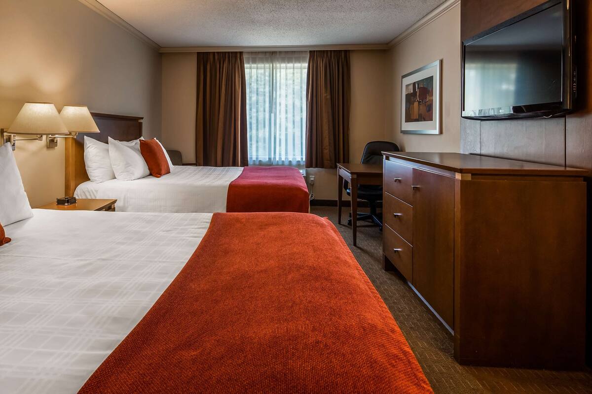 A hotel room with two beds, a desk, a chair, a TV, and a wardrobe.