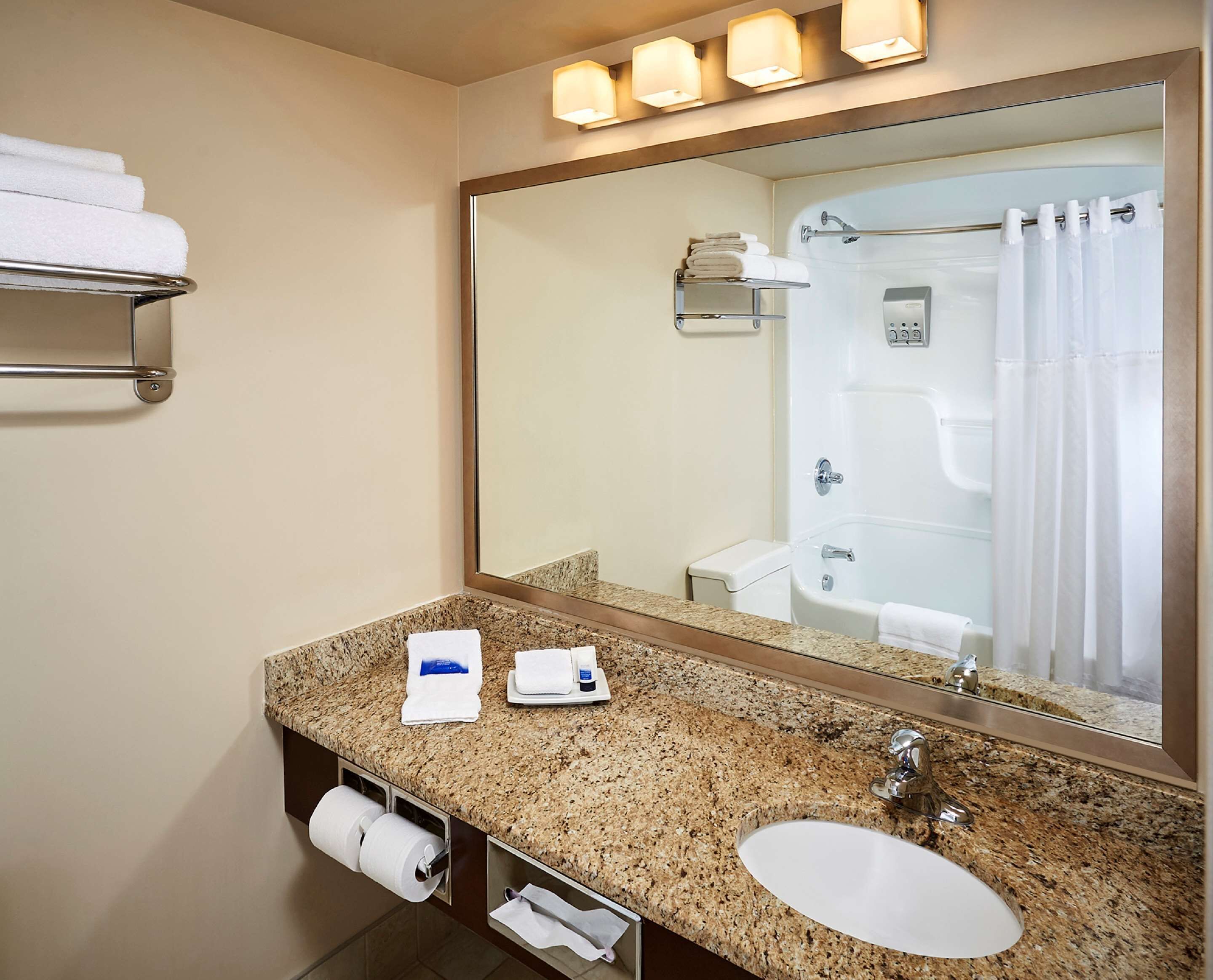 Un baño con encimera de granito, un lavabo, un espejo, un perchero para toallas y una cortina de ducha.