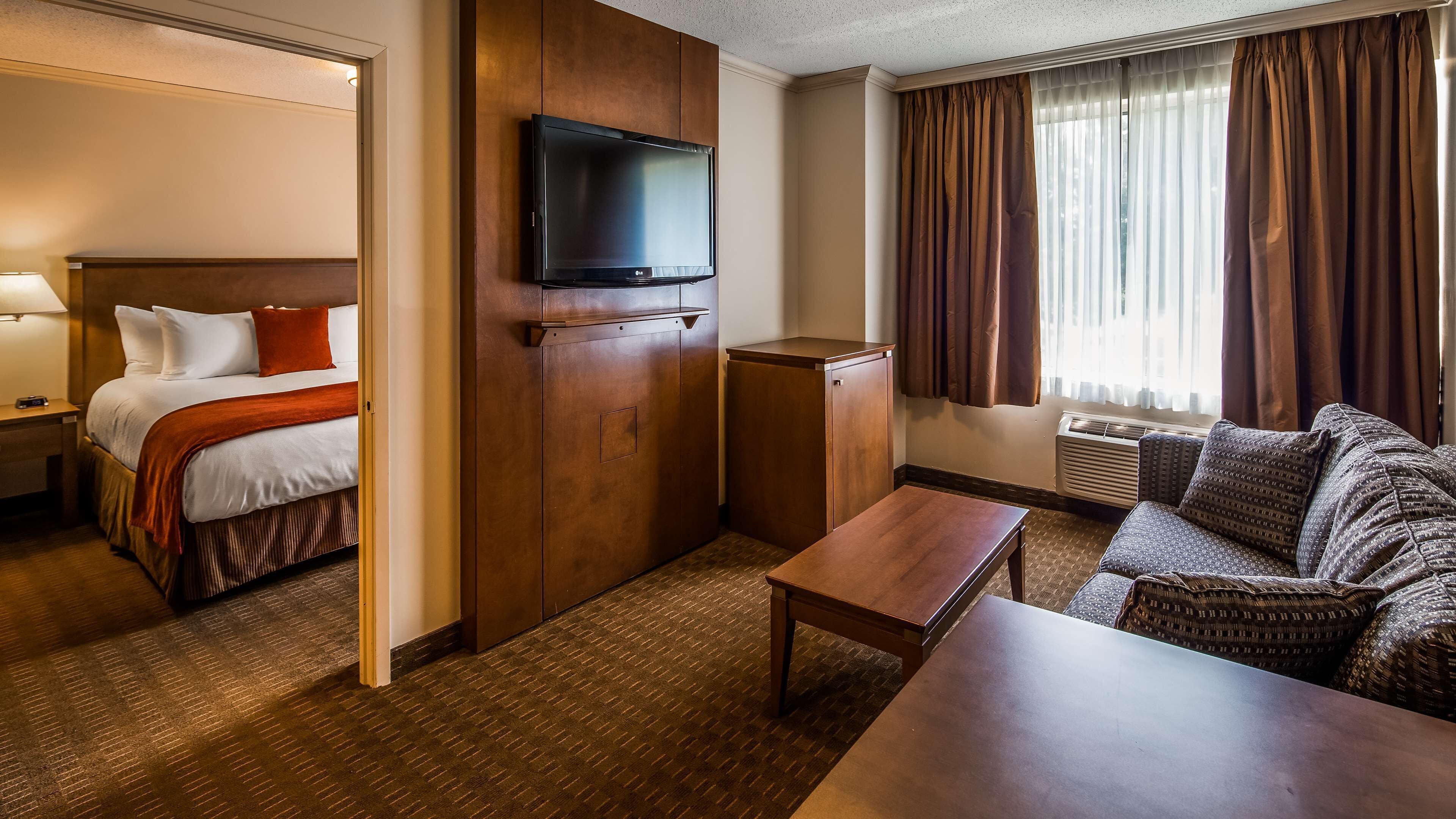 A hotel room with a bed, a television, a sofa, a table, and a window with curtains.