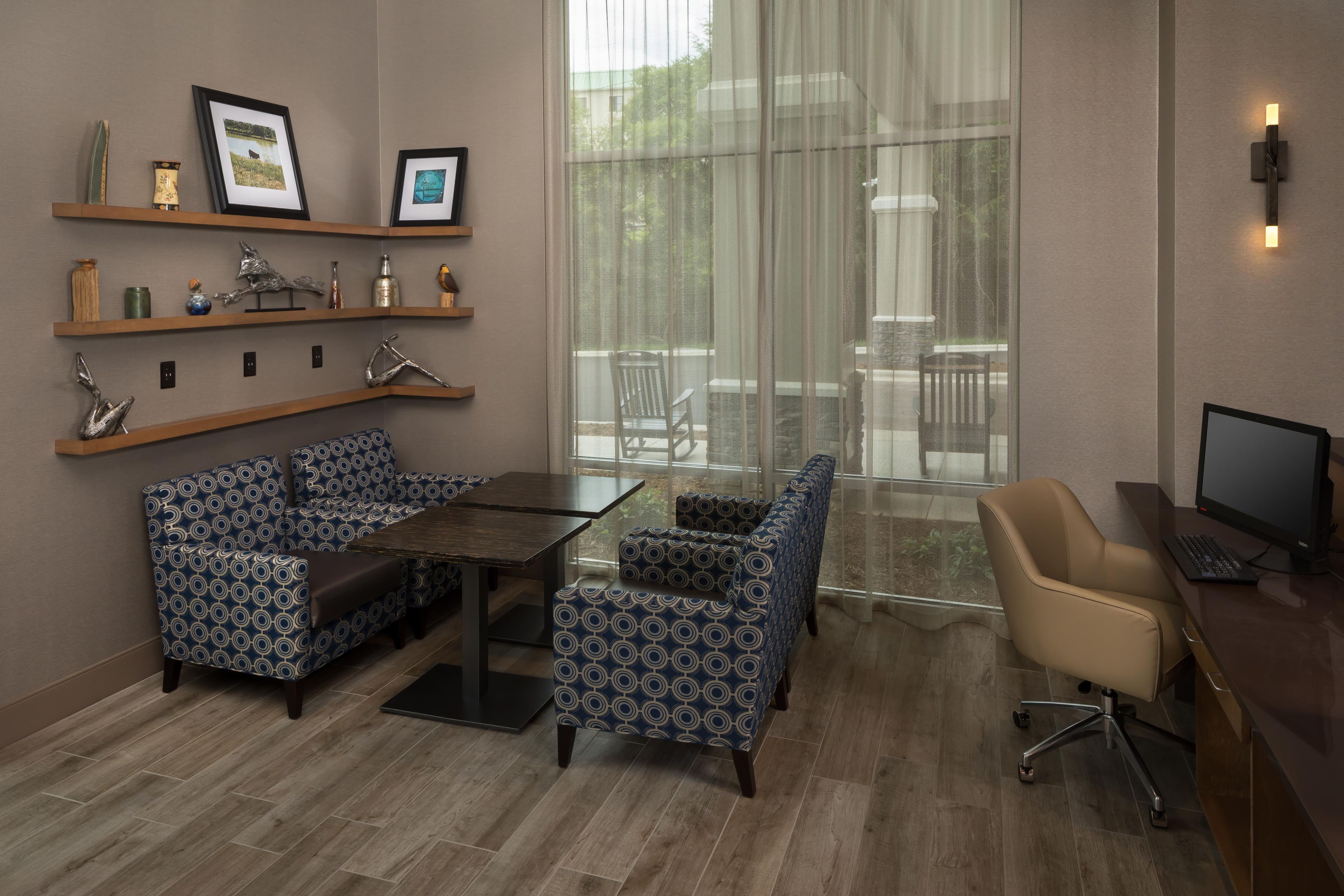 A modern hotel room with a dining area, a computer desk, and a large window with a view of the outdoors.