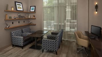 A modern hotel room with a dining area, a computer desk, and a large window with a view of the outdoors.