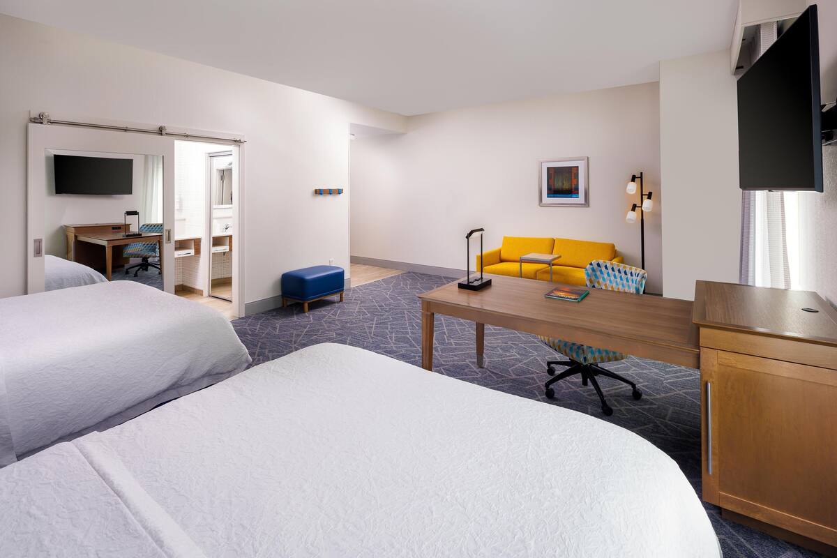 Een hotelkamer met twee bedden, een bureau, een stoel, een bank, een televisie en een badkamer.