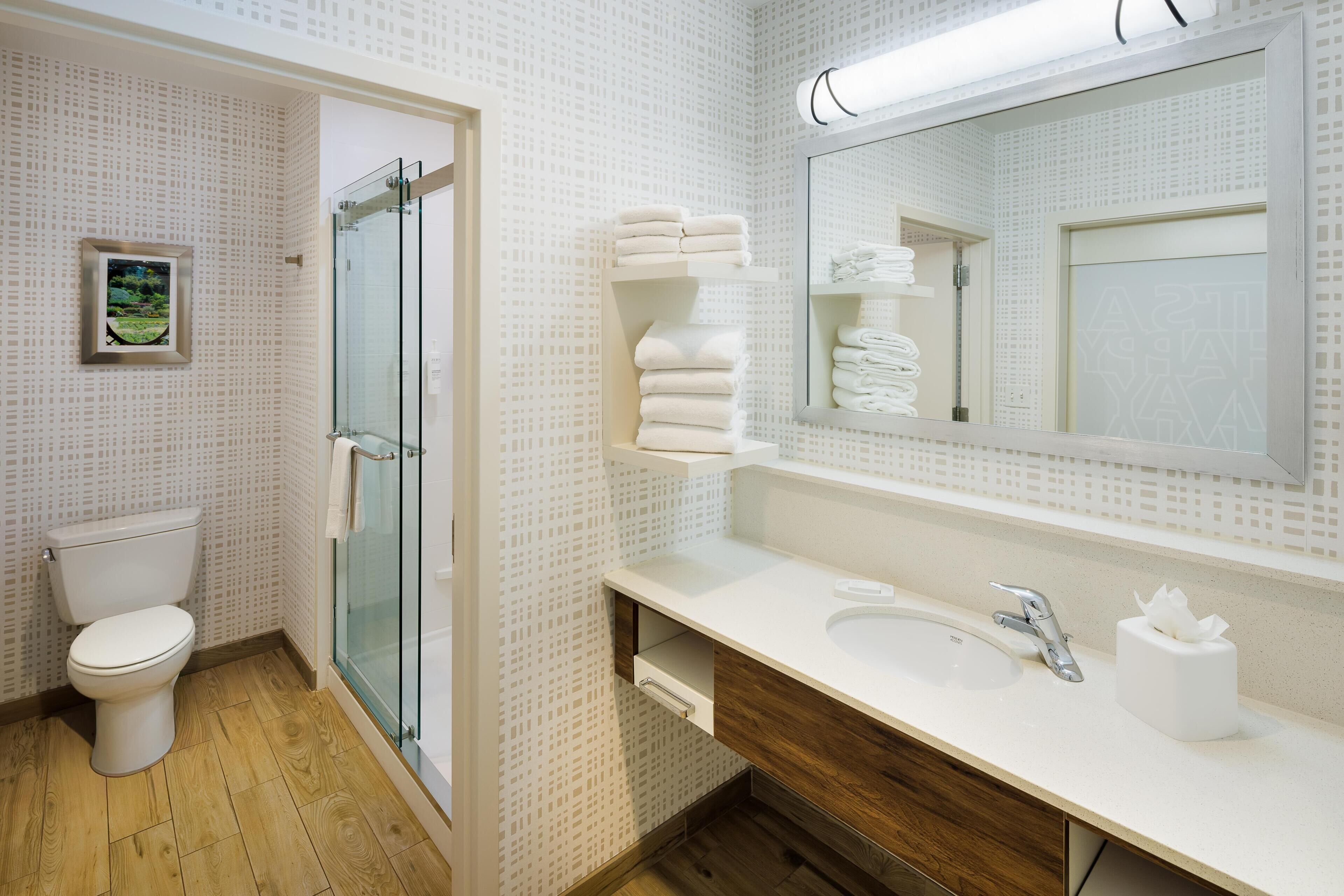 Un baño con inodoro, cabina de ducha de vidrio, lavabo blanco y espejo con toallas.