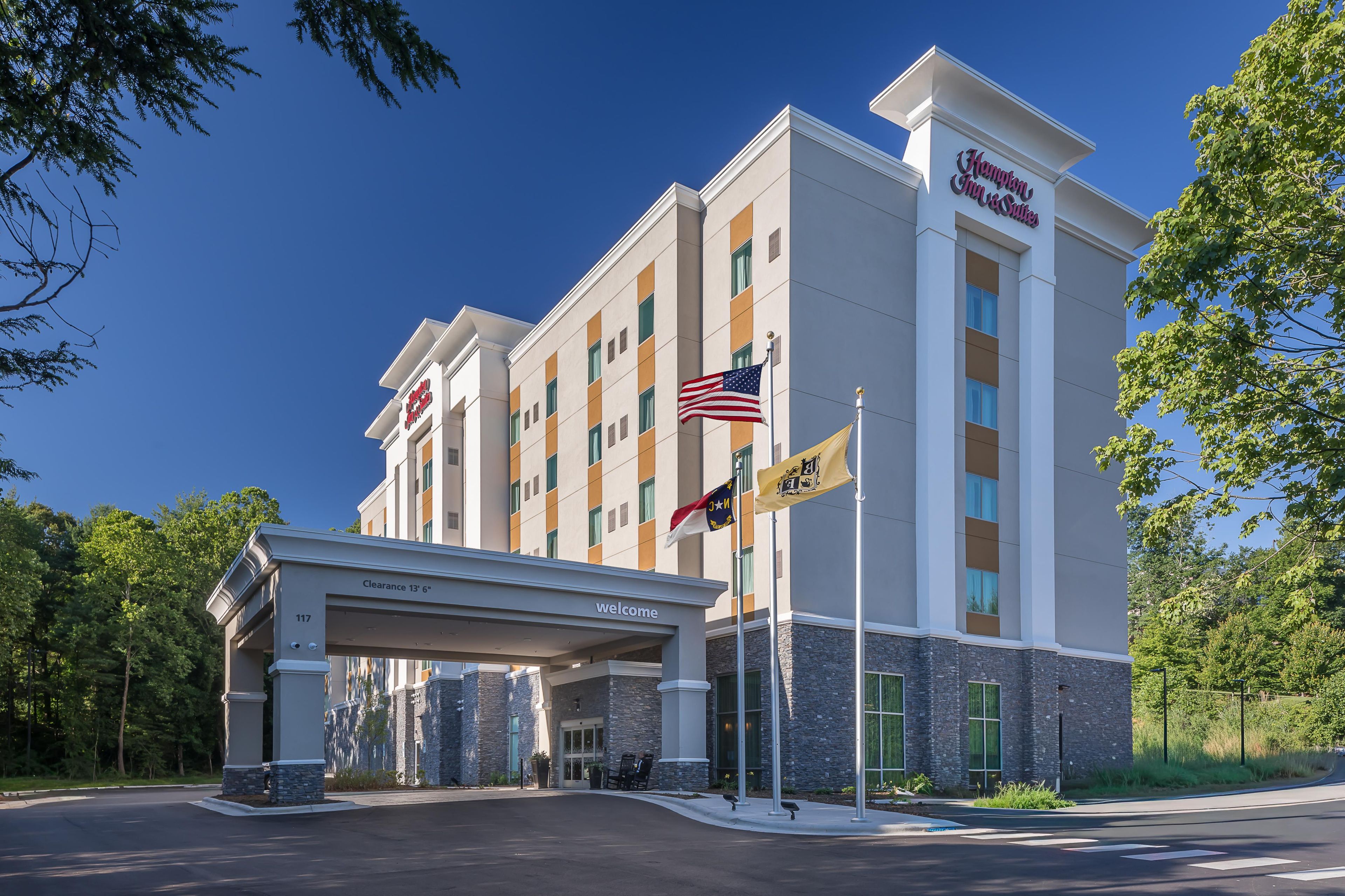 A Hampton Inn & Suites hotel with a clear sky, a welcoming entrance, and multiple flags.