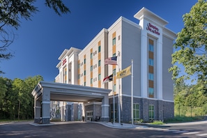 Un hotel Hampton Inn & Suites con cielo despejado, una entrada acogedora y varias banderas.