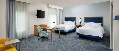 A hotel room with two beds, a desk, a chair, a TV, and a window with curtains.