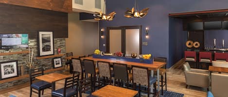 Un comedor moderno con una mesa y sillas de madera, un espejo grande sobre la mesa, y una zona de cocina con toallas rojas.