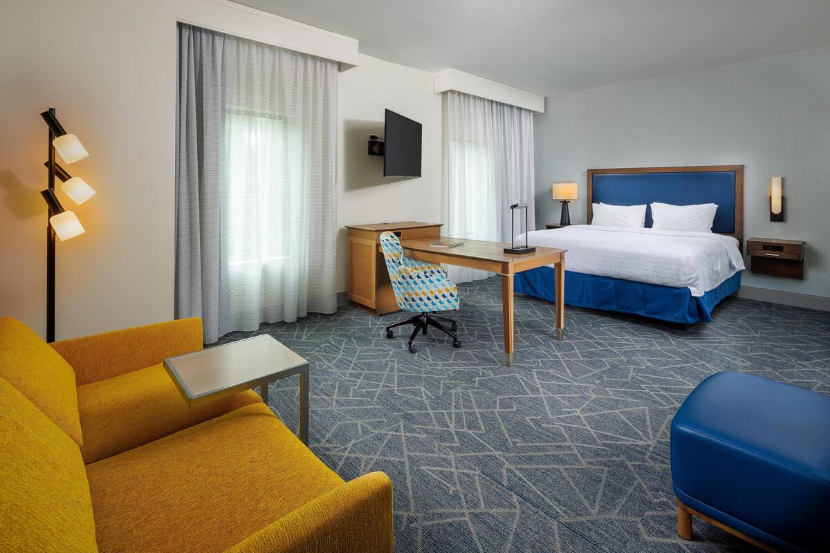 Een hotelkamer met een bed, een bureau, een stoel, een bank, een televisie en een lamp.