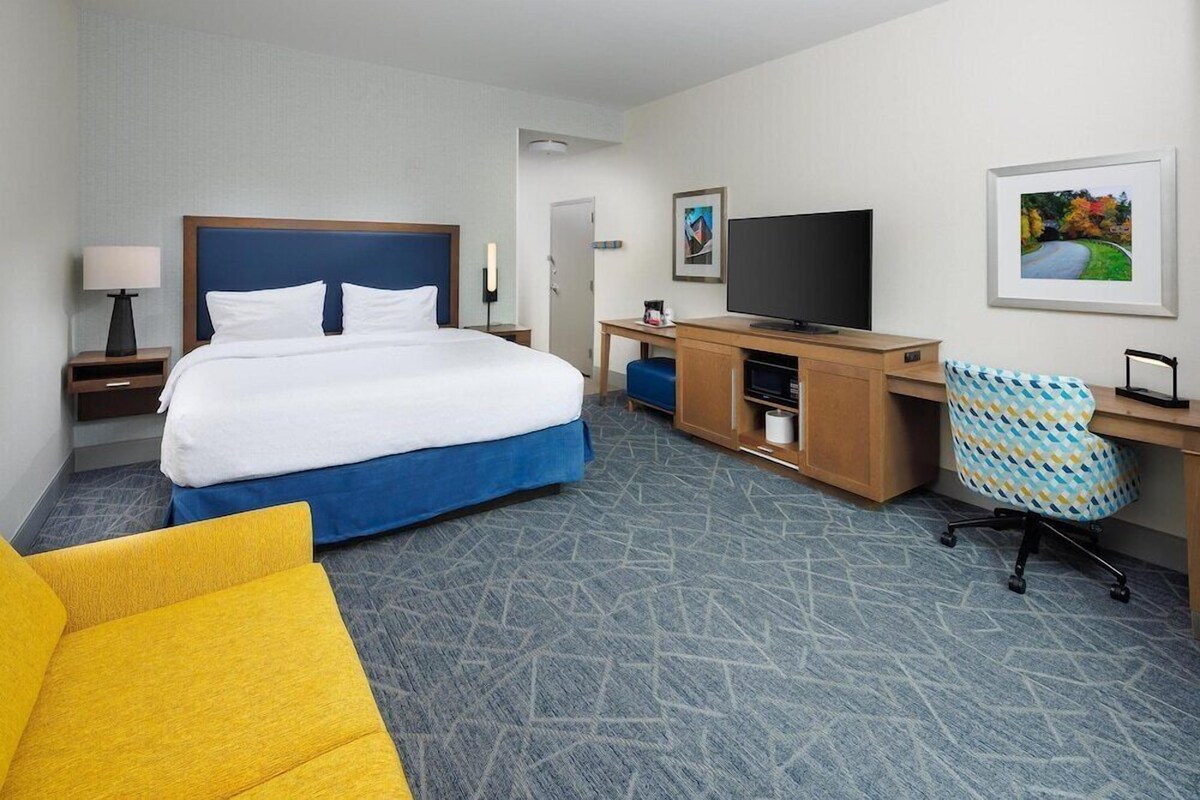 A hotel room with a bed, a desk, a television, a chair, and a picture on the wall.