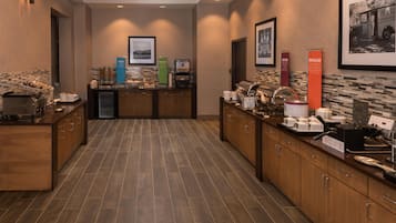A hotel kitchen with a buffet setup, including a coffee machine, a water dispenser, and various food items.