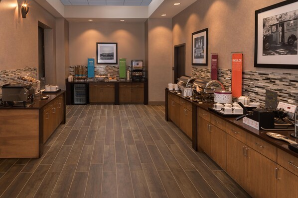 A hotel kitchen with a buffet setup, including a coffee machine, a water dispenser, and various food items.