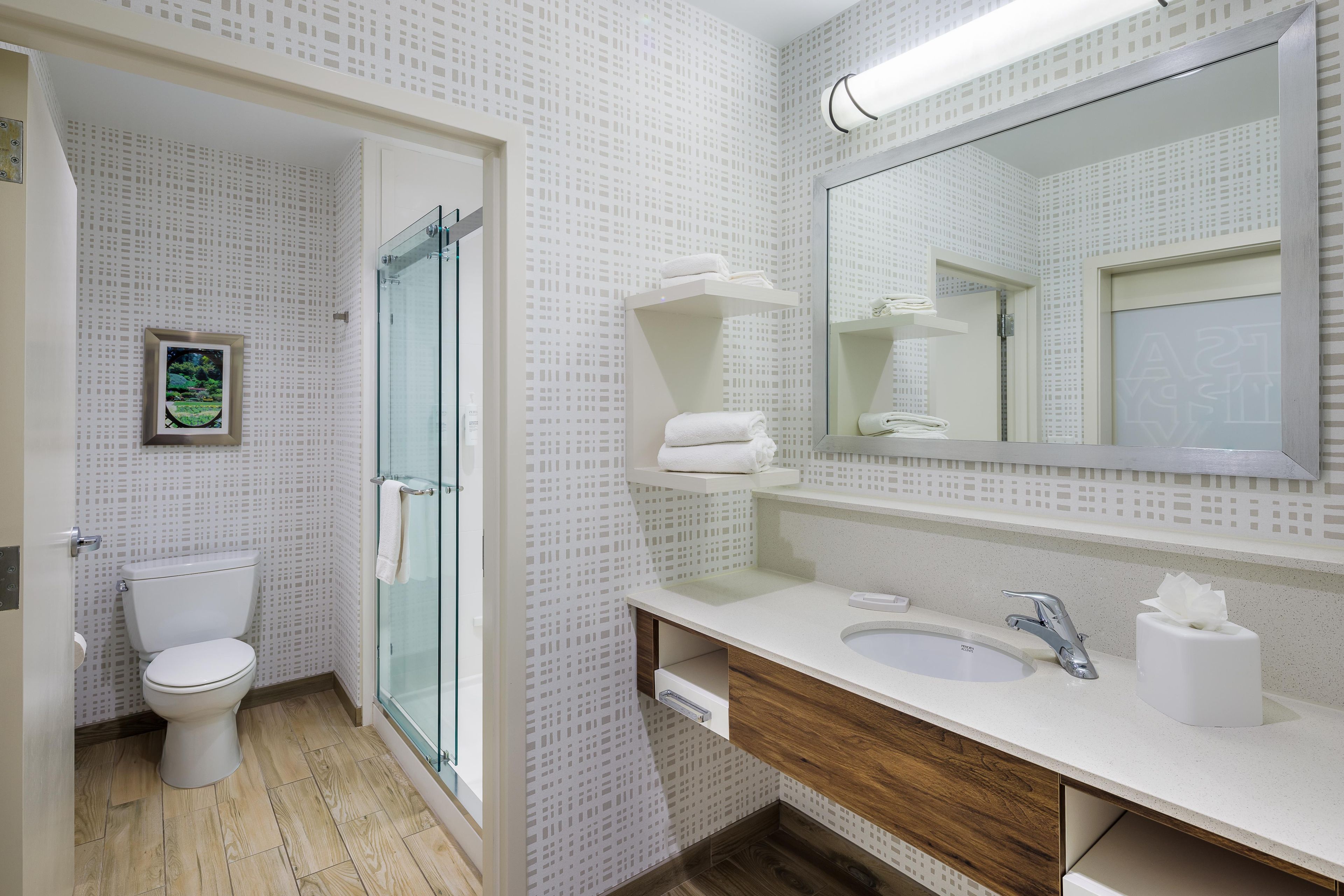 Un baño moderno con inodoro, ducha de vidrio y tocador con lavamanos y espejo.