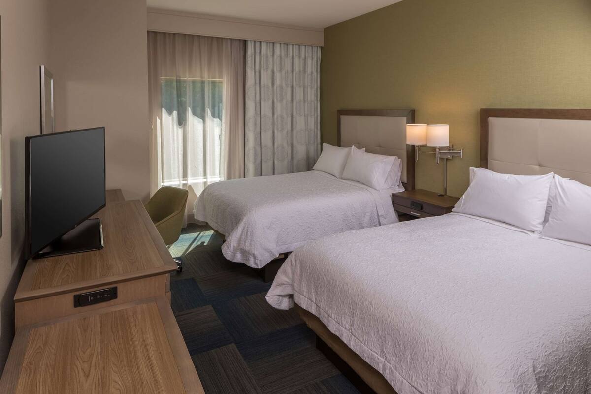 Een hotelkamer met twee bedden, een televisie, een bureau en een stoel.
