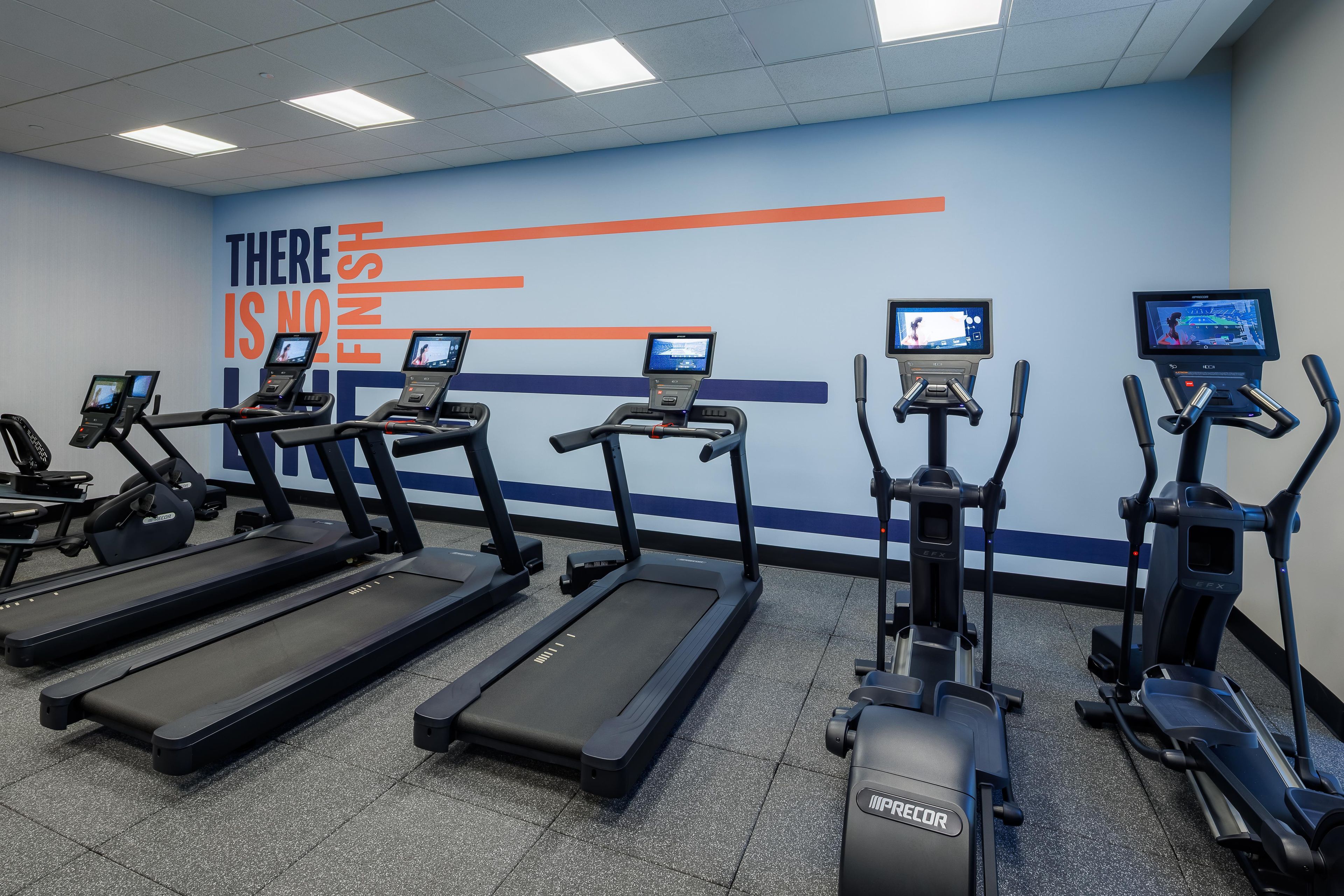 Une salle de sport équipée de tapis de course et d’appareils elliptiques, agrémentée de décorations murales inspirantes et dotée d’écrans numériques.