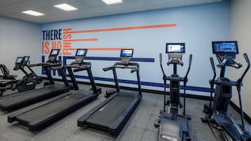 A gym with treadmills and elliptical machines, motivational wall art, and digital screens.