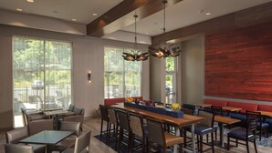 A modern dining area with a long wooden table, multiple seating options, and large windows offering views of the outdoors. - Hampton Inn & Suites Asheville Biltmore Village (Asheville)