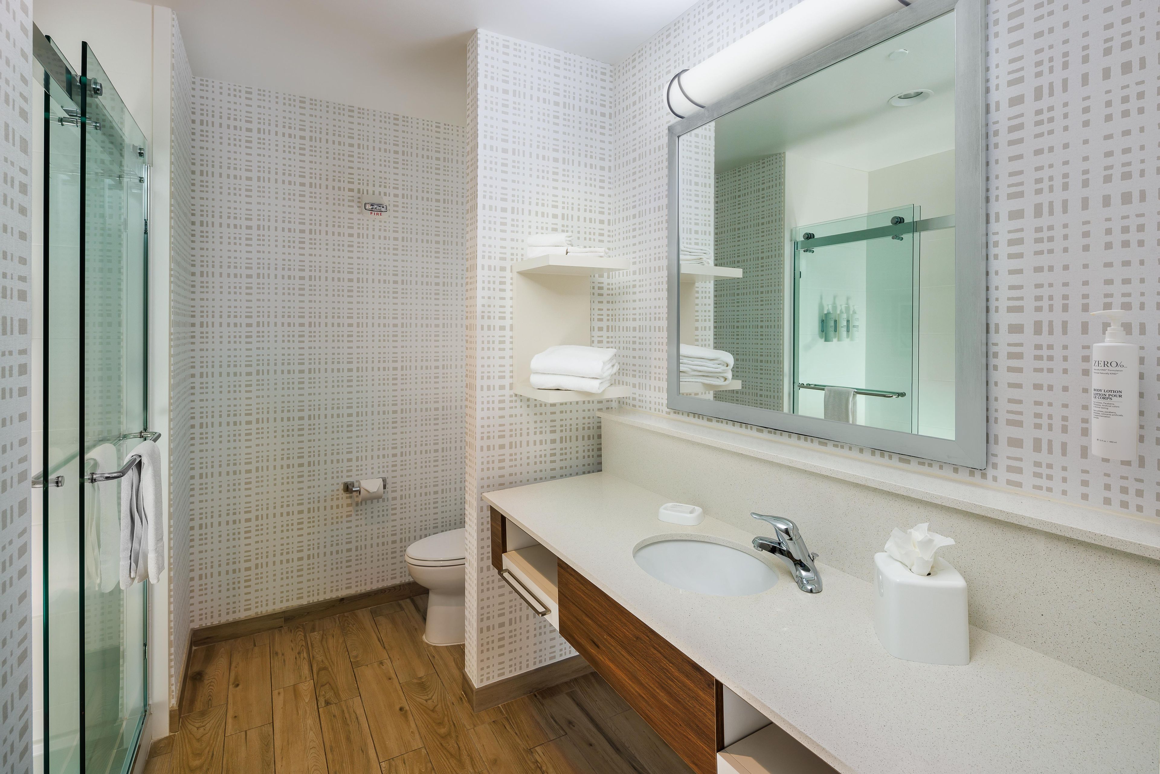 A modern bathroom with a glass shower enclosure, a wooden floor, a white sink with a mirror, and a toilet.