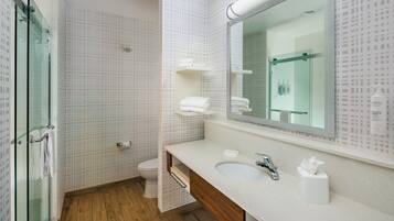 A modern bathroom with a glass shower enclosure, a wooden floor, a white sink with a mirror, and a toilet.