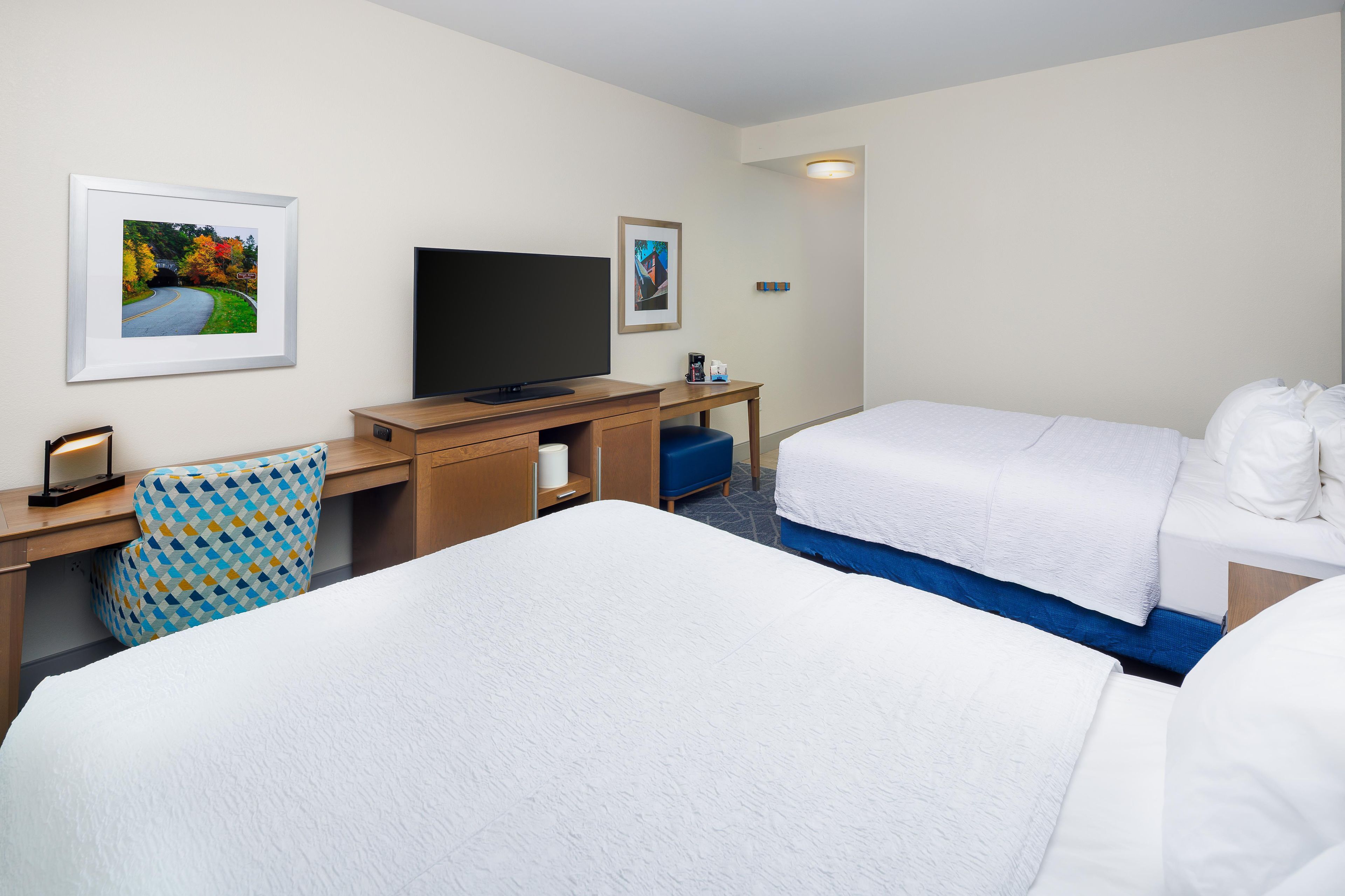 Ett hotellrum med två sängar, ett skrivbord med en tv och inramade tavlor på väggen.