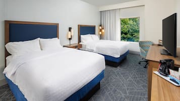 A hotel room with two beds, a desk with a coffee maker, a TV, and a window with a view of trees.