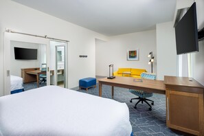Habitación de hotel con cama, escritorio, silla, sofá, televisor y ventana.