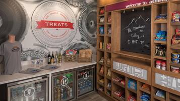 A snack bar with a 'TREATS' sign, shelves stocked with snacks, a chalkboard with a quote, and a refrigerator with beverages.