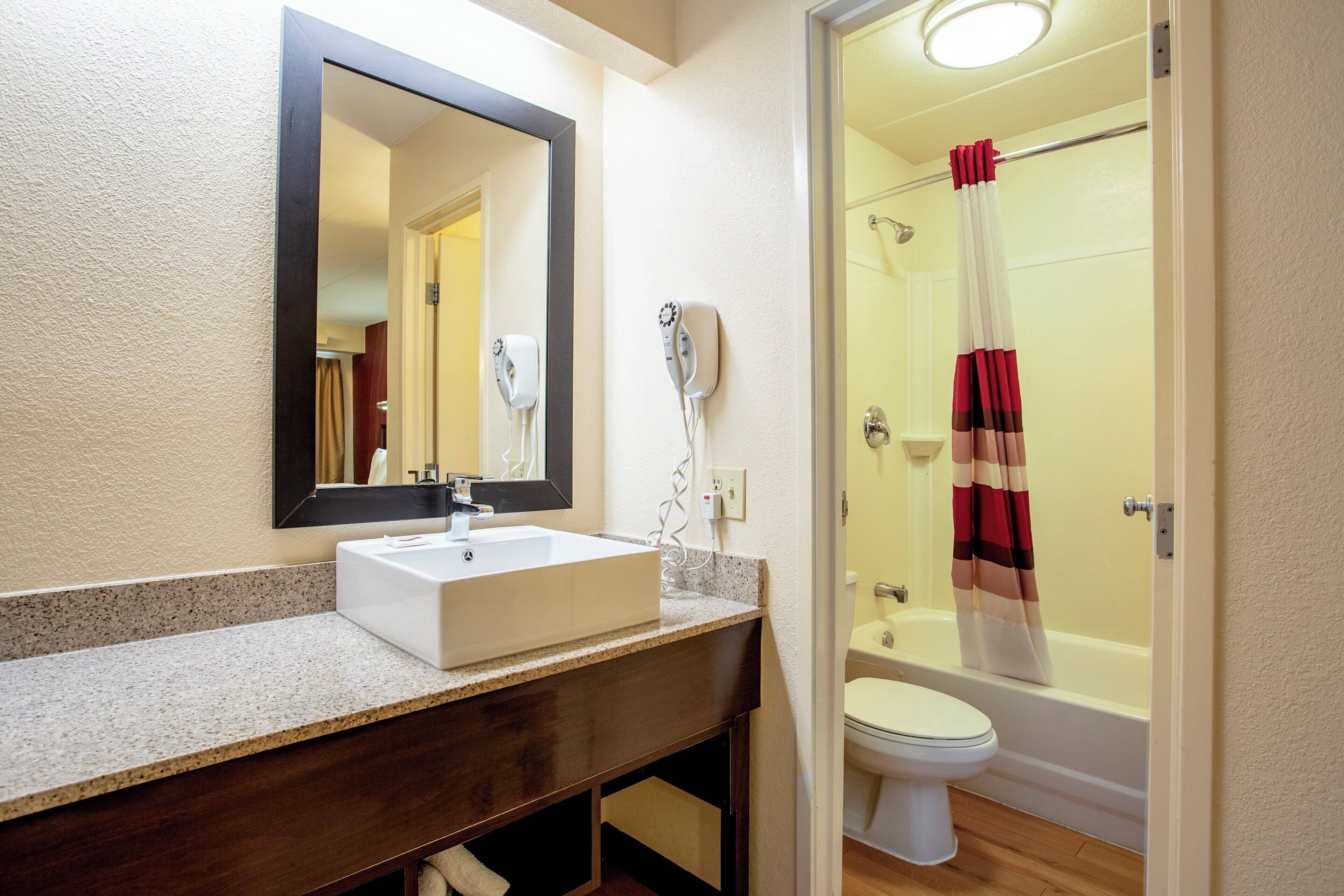 Un baño con lavamanos blanco, espejo y ducha con cortina a rayas rojas y blancas.