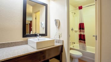 Un baño con lavamanos blanco, espejo y ducha con cortina a rayas rojas y blancas.
