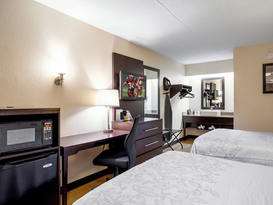 A hotel room with a desk, a television, a bed, a mirror, and a coffee machine.