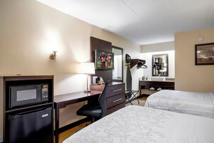 A hotel room with a desk, a television, a bed, a mirror, and a coffee machine.