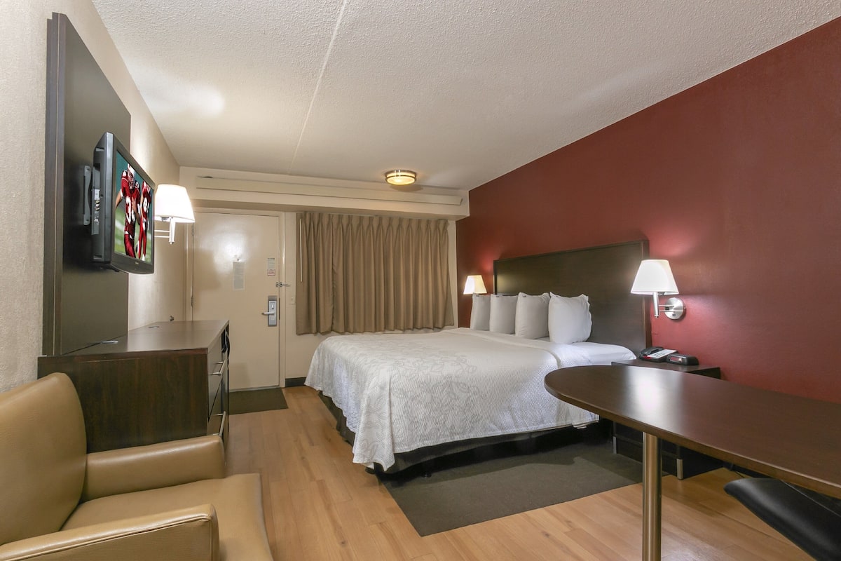 A hotel room with a bed, bedside tables, a desk, a chair, a TV, and a lamp.