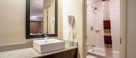 Une salle de bain avec un lavabo blanc, un miroir, un sèche-cheveux, une douche et des toilettes.