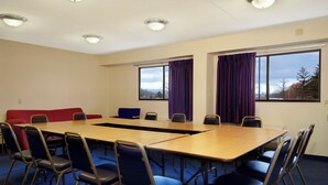 Un salón de conferencias con una larga mesa, sillas, un sofá rojo y ventanas con cortinas.