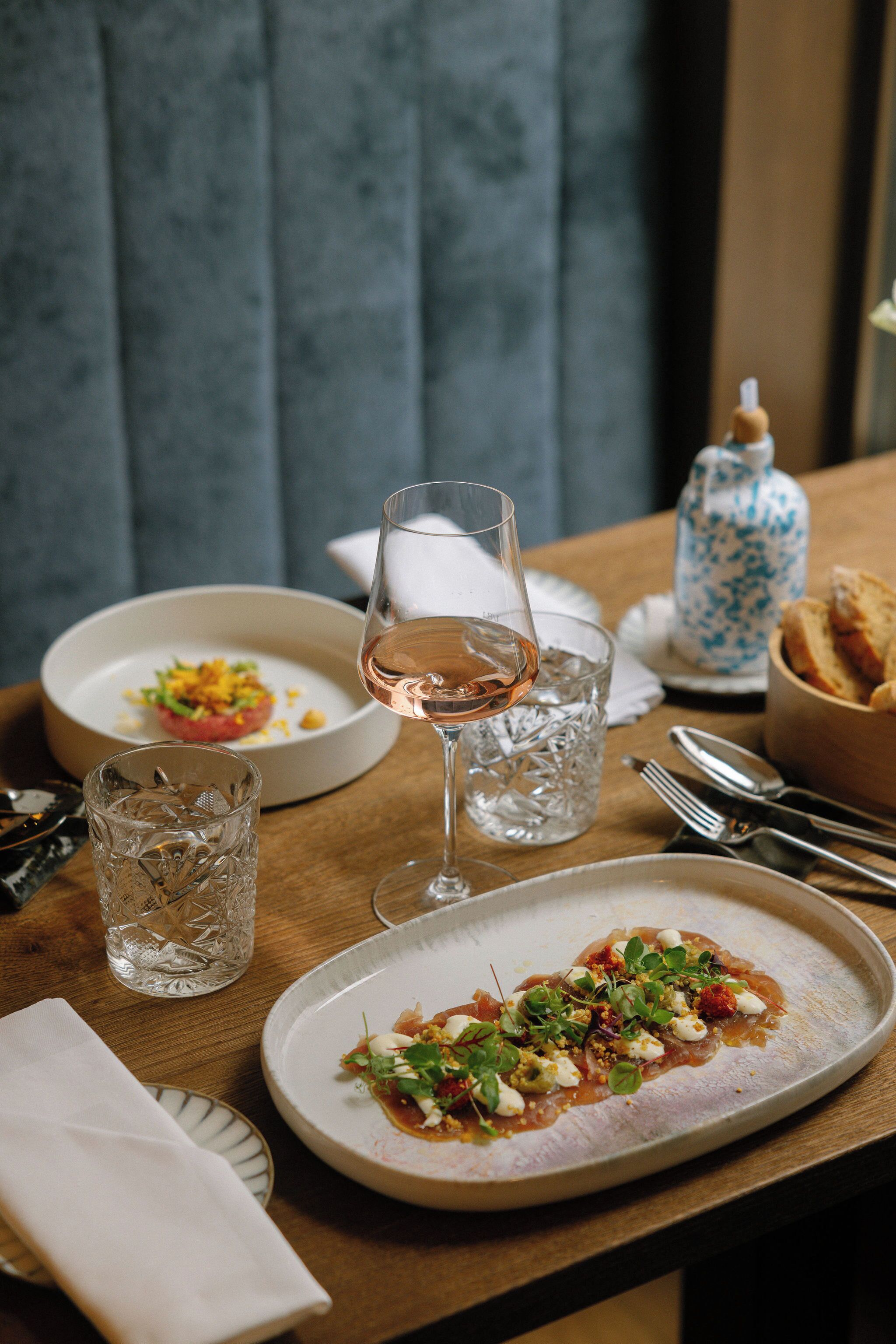Une table à manger avec des assiettes remplies de nourriture, un verre de vin et un verre d’eau.