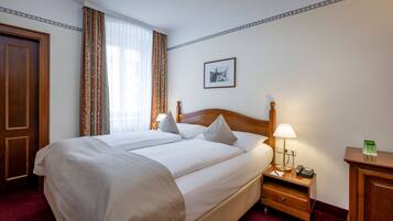 A hotel room with a large bed, a bedside table with a lamp, a phone, and a picture on the wall.