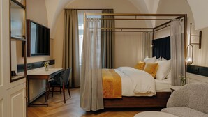 Una cama con dosel, un escritorio con una silla, una mesa redonda y un televisor montado en la pared.