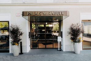 Der Eingang eines Hotels namens 'Palais Mirabel' mit Glastür, zwei Topfpflanzen und einem Schild über der Tür.