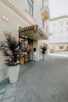 A hotel entrance with a glass facade, a sign reading 'IMLAUER PALAS MIRABEL,' and potted plants on the sidewalk.