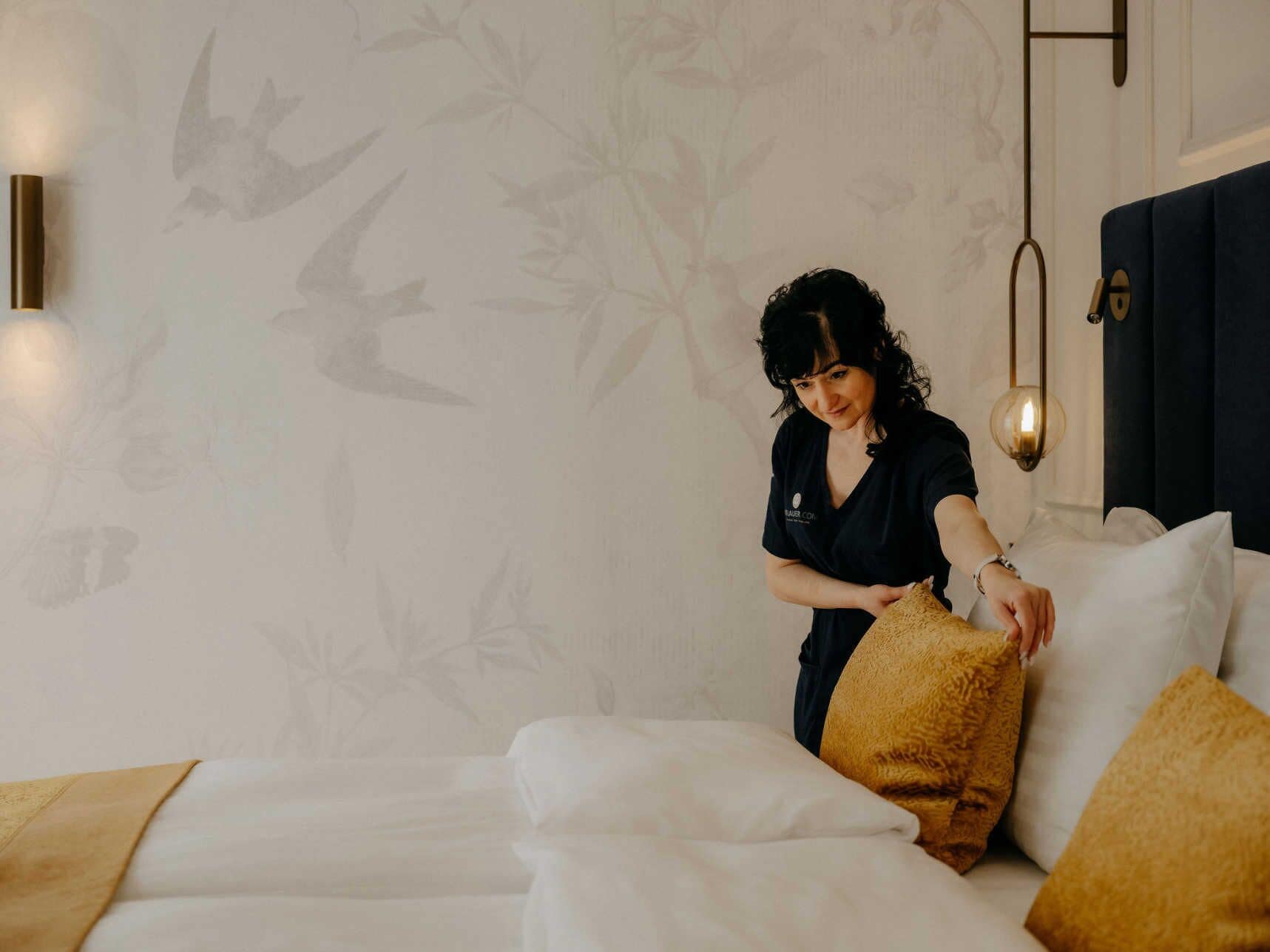 A room with a bed, a wall with a bird pattern, and a hanging light fixture.