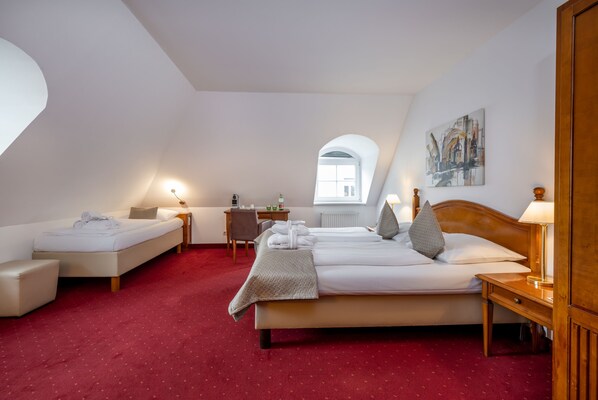Une chambre d’hôtel avec un tapis rouge, deux lits, un bureau, une chaise, une lampe et un tableau au mur.